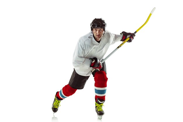 Young male hockey player with the stick on ice court and white background.