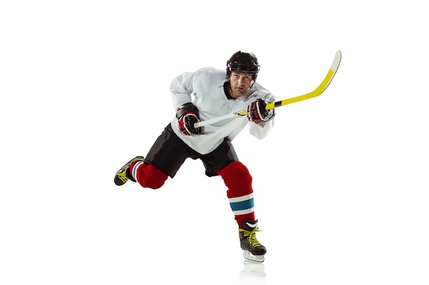 Young male hockey player with the stick on ice court and white wall. Sportsman wearing equipment and helmet practicing