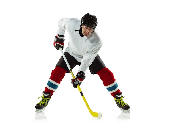 Young male hockey player with the stick on ice court and white wall