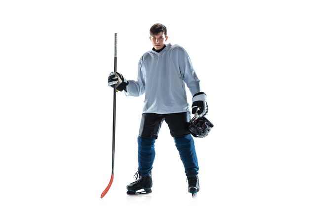 Young male hockey player with the stick on ice court and white wall