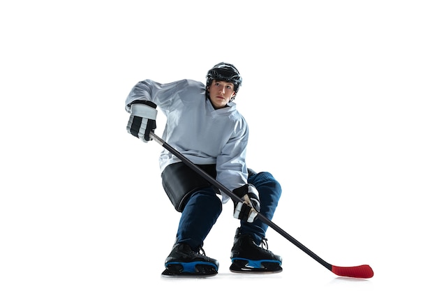 Young male hockey player with the stick on ice court and white wall