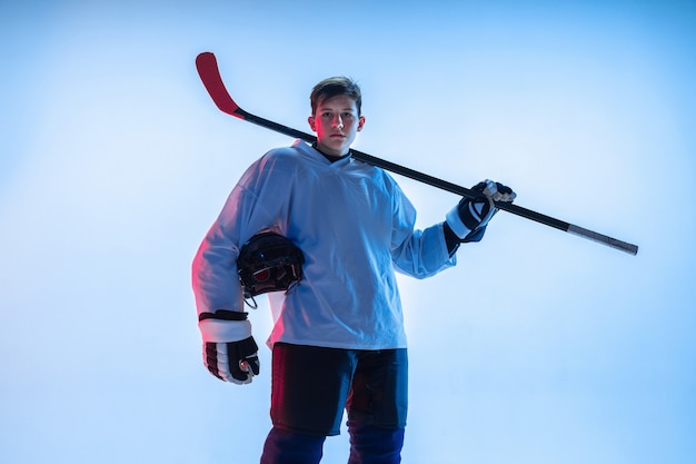 Giovane giocatore di hockey maschio con il bastone sul muro bianco in luce al neon