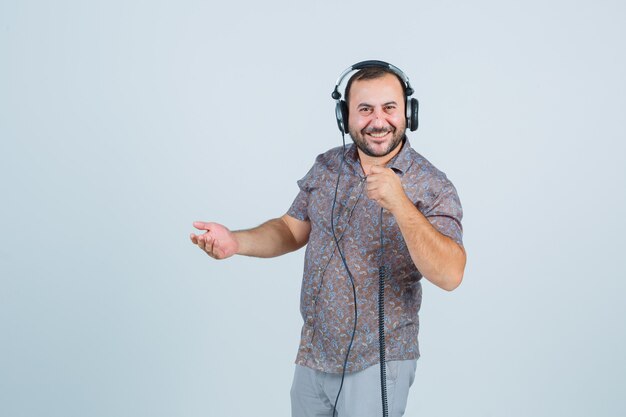 カジュアルなシャツ、ズボン、エネルギッシュな正面図でカメラに笑みを浮かべながら携帯電話のケーブルを保持している若い男性。
