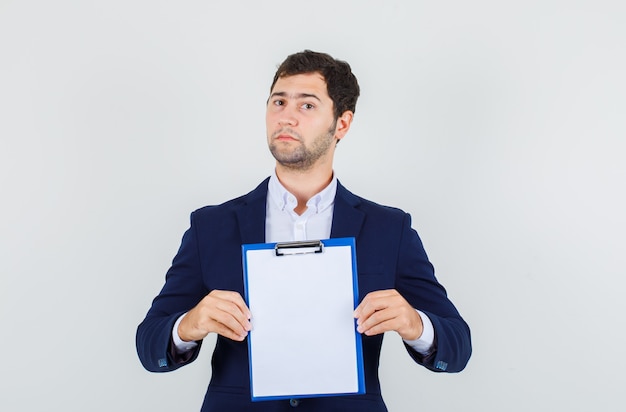 Young male holding clipboard in suit and looking strict. front view.