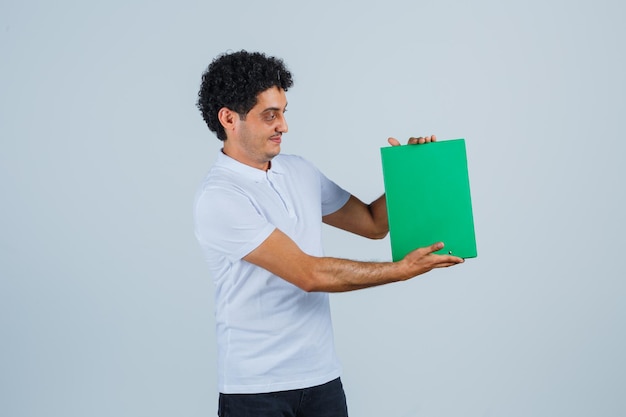 Free photo young male holding clipboard in white t-shirt, pants and looking cheerful. front view.