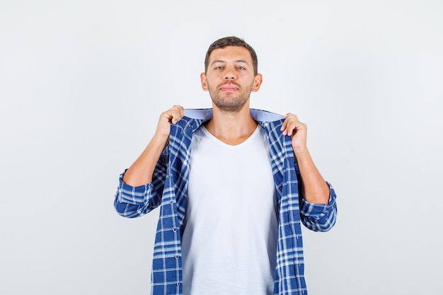 Young male holding collar of clothes in shirt and looking confident , front view.