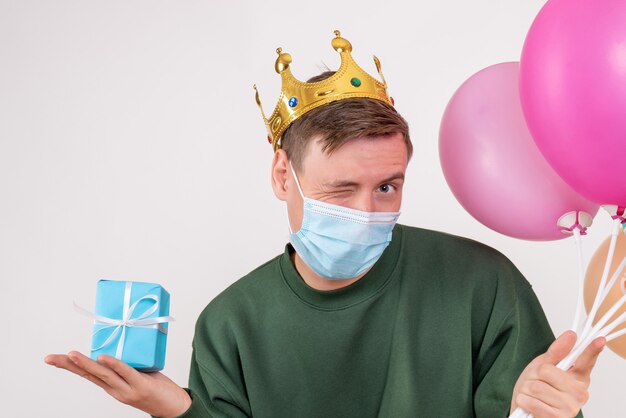 young male holding colorful balloons and little present on white