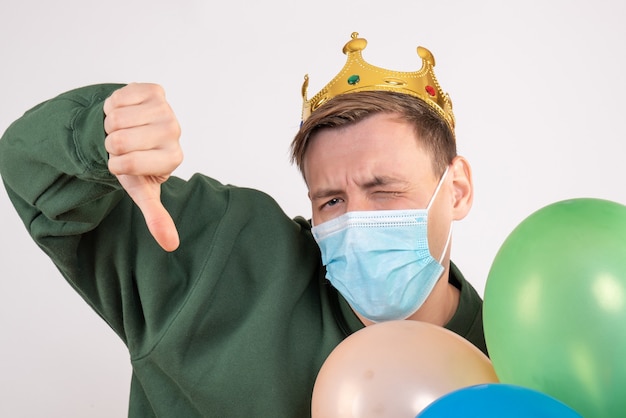 Free photo young male holding colorful balloons in mask on white