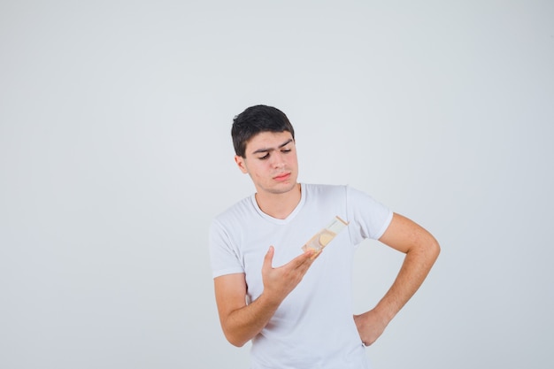 Young male holding euro banknote in t-shirt and looking careful , front view.