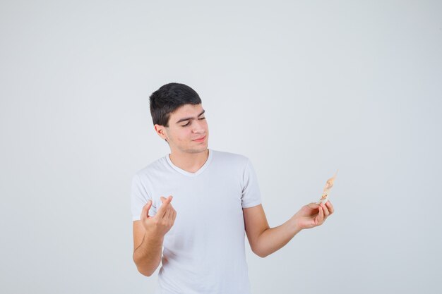 Young male holding eurobanknote, pointing up in t-shirt and looking cheery. front view.