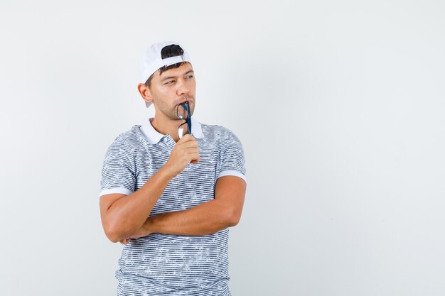 Young male holding glasses while looking away in t-shirt and cap and looking hopeful 