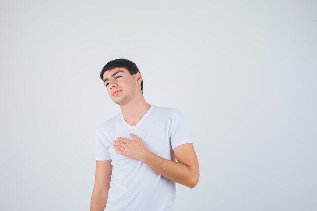 Young male holding hand on chest in t-shirt and looking careful. front view.