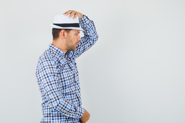 Young male holding hand on his hat in checked shirt