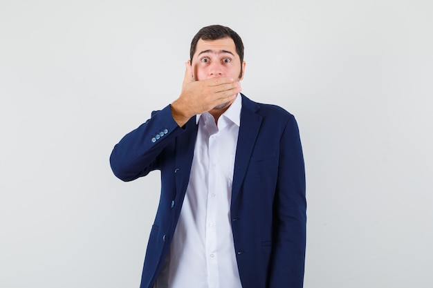 Young male holding hand on mouth in shirt