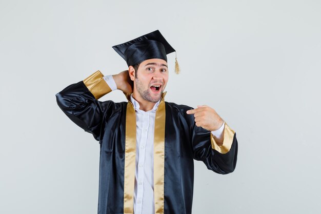 Foto gratuita giovane maschio che tiene la mano sul collo, indicando se stesso nella vista frontale dell'uniforme laureata.