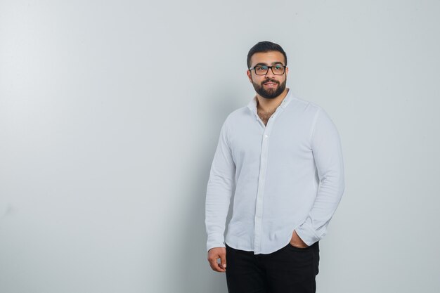 Young male holding hand in pocket in white shirt, pants and looking handsome