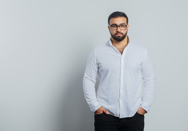 Young male holding hands in pockets in white shirt, pants and looking elegant