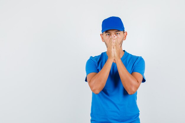 Young male holding hands in praying gesture in blue t-shirt
