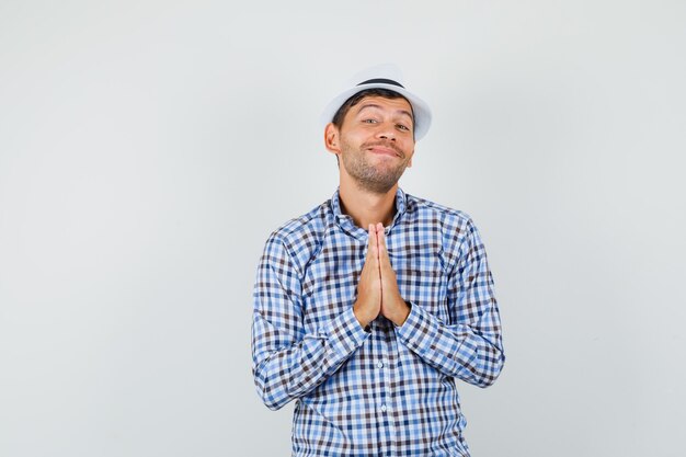 Молодой мужчина, взявшись за руки в молитвенном жесте в клетчатой рубашке