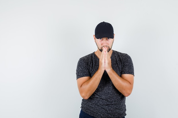 Young male holding hands in praying gesture in t-shirt and  cap