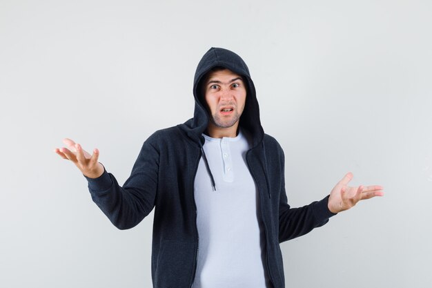 Young male holding hands in questioning gesture in t-shirt, jacket and looking nervous , front view.