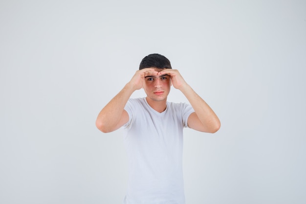 Young male holding hands to see clearly in t-shirt and looking focused. front view.