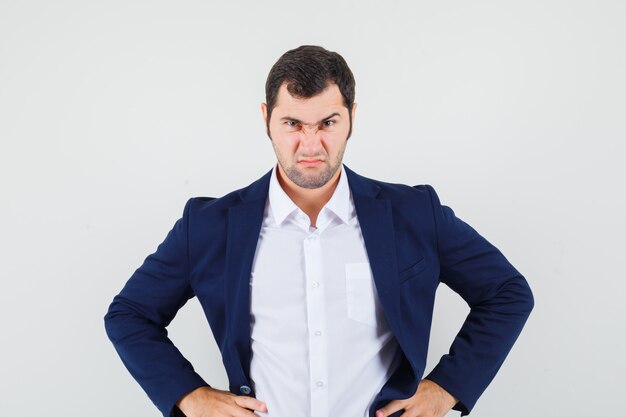 Young male holding hands on waist in shirt and jacket and looking gloomy