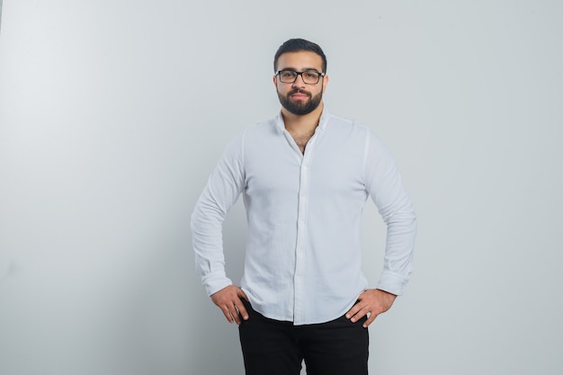 Young male holding hands on waist in white shirt, pants and looking handsome