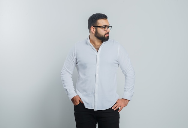 Young male holding hands on waist in white shirt, pants and looking handsome