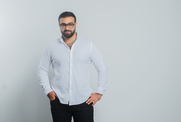 Young male holding hands on waist in white shirt, pants and looking handsome