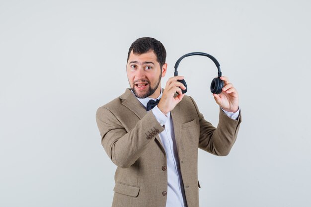 Young male holding headphones to wear in suit front view.