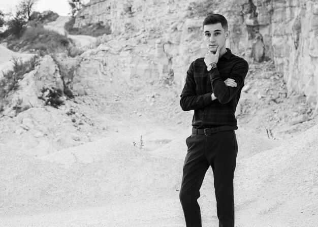 Young male holding his chin under the sunlight with rocks and cliffs on the