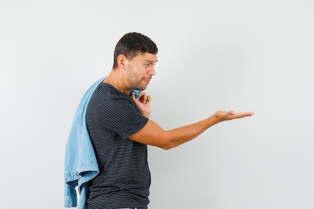 Young male holding jacket on back looking at empty palm in t-shirt and looking depressed