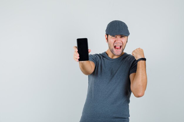 Молодой мужчина держит мобильный телефон в кепке футболки и выглядит счастливым