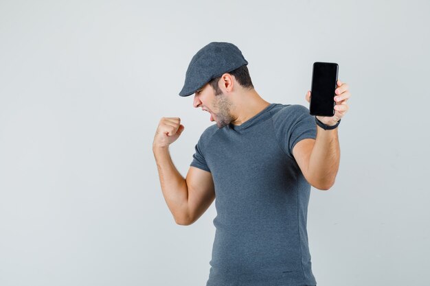 Young male holding mobile phone in t-shirt cap and looking lucky