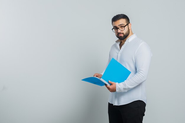 Young male holding opened folder in white shirt, pants and looking handsome