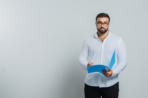 Young male holding opened folder in white shirt, pants and looking handsome