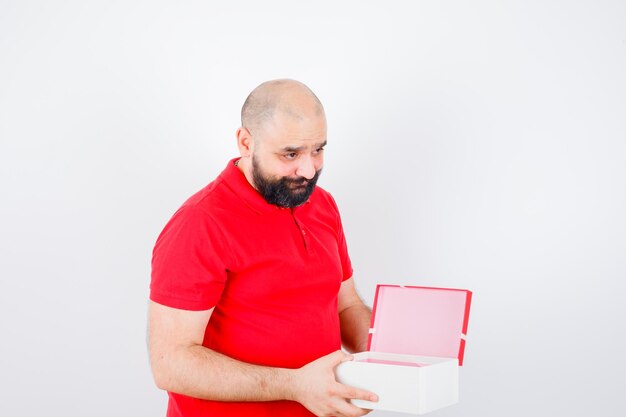 Young male holding opened gift box in red t-shirt and looking shy , front view.