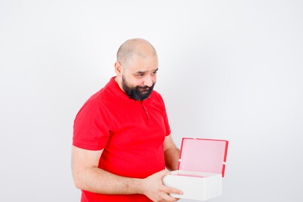 Молодой самец открыл подарочную коробку в красной футболке и выглядел застенчивым, вид спереди.
