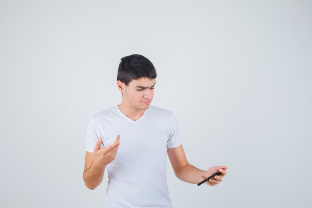 Young male holding phone while pointing aside in t-shirt and looking focused. front view.