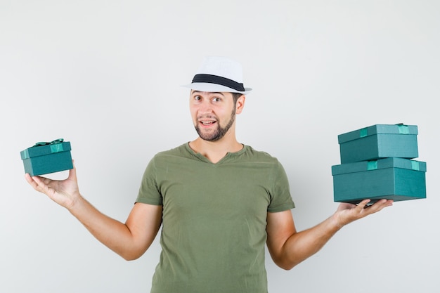 Young male holding present boxes in green t-shirt and hat and looking cheerful