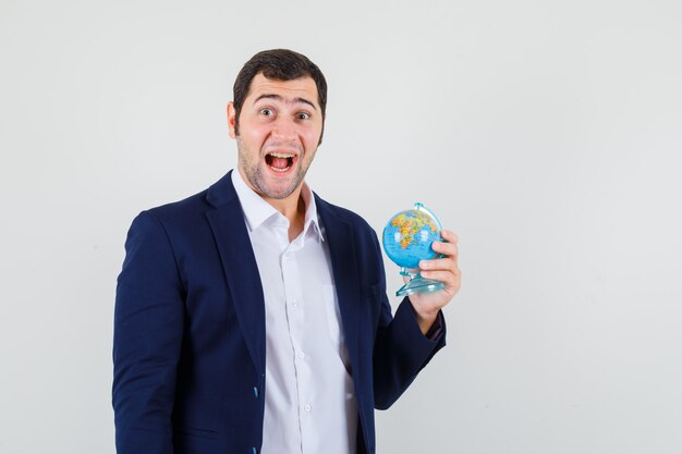 Young male holding school globe in shirt and jacket and looking glad