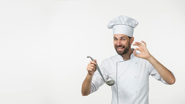 Young male holding soup from ladle making tasty sign isolated on white background