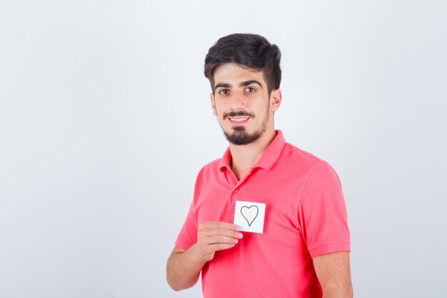 Young male holding sticky note while looking away in t-shirt and looking blissful , front view.