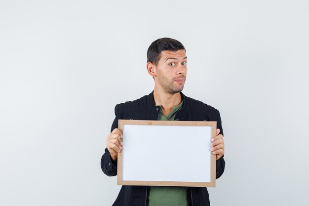 Young male holding white board in t-shirt, jacket front view.