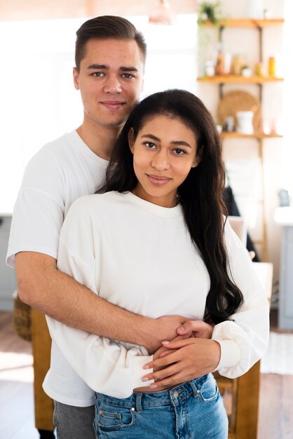 Young male hugging ethnic girlfriend and looking at camera