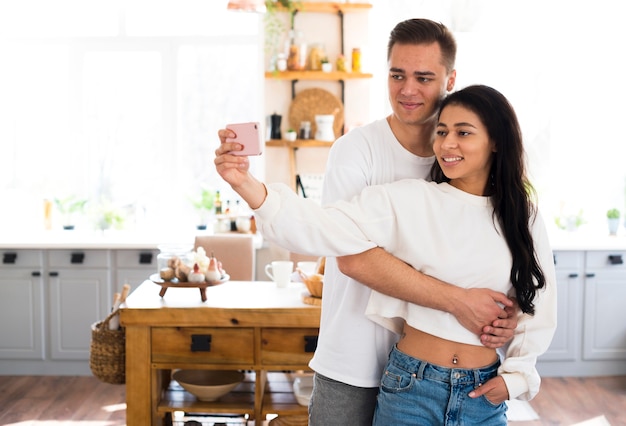 Free photo young male hugging ethnic girlfriend taking selfie at home