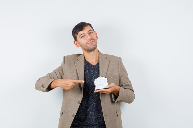 मुफ़्त फोटो young male in jacket, t-shirt pointing at house model and looking cheerful , front view.