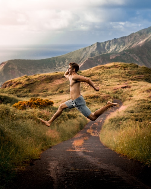 햇빛과 흐린 하늘 아래 산으로 둘러싸인 필드에서 점프하는 젊은 남성