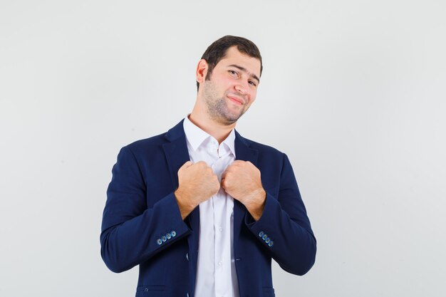 Young male keeping fists on chest in shirt and jacket and looking confident